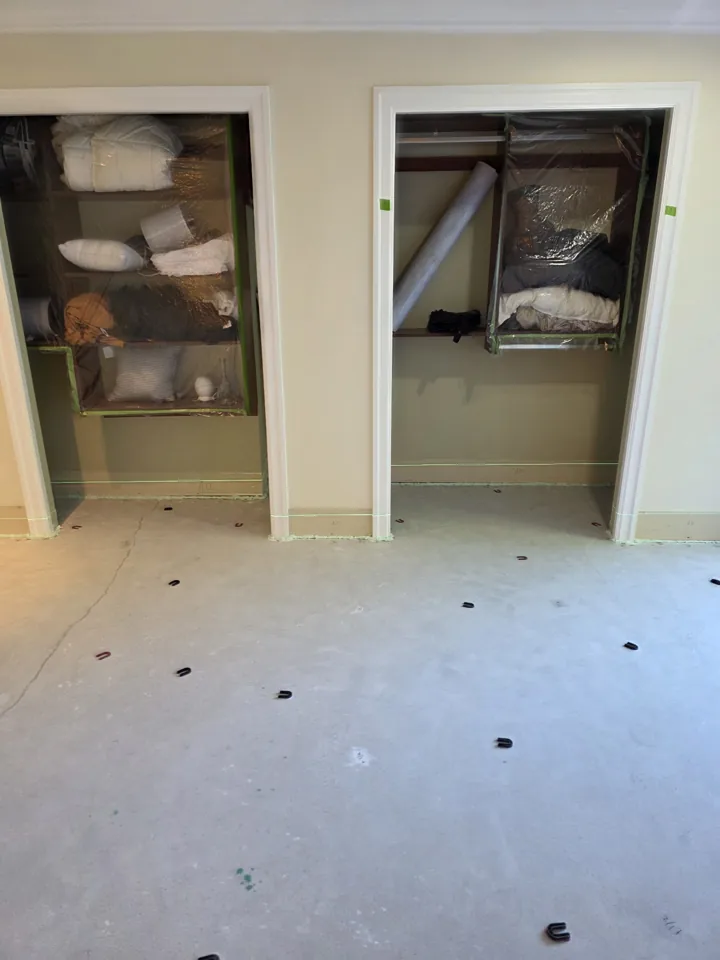 The same Westport bedroom after grinding, before priming, with a laser, height reference shims and poly covering the closet contents