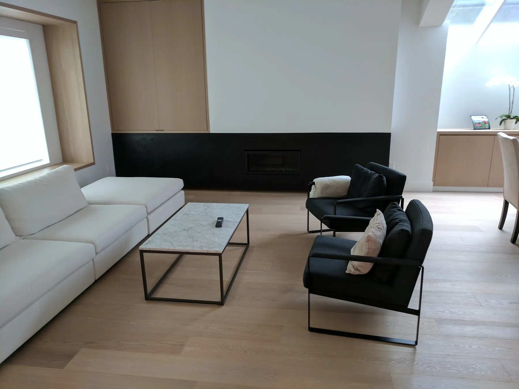 Light oak floor beneath a white sofa and black chairs in a modern Vancouver living room
